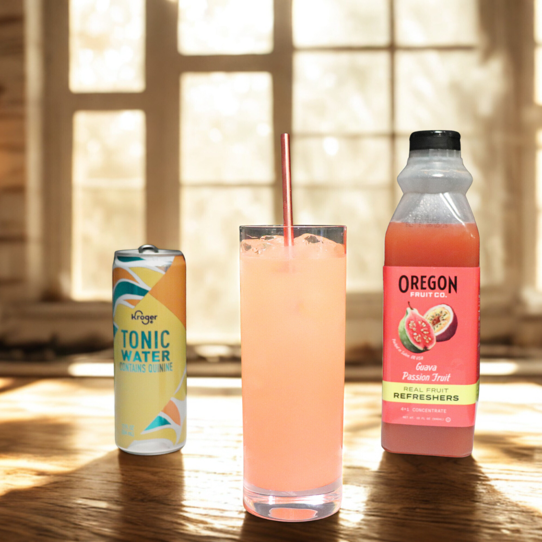Clear glass of pink beverage next to can of Tonic and bottle of Oregon Fruit Guava Passion Fruit Refresher, in front of wall of windows