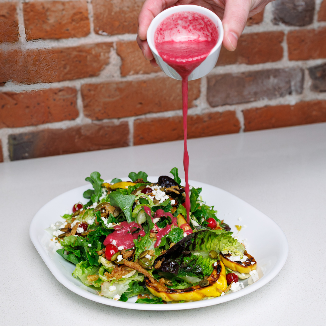 bright cranberry thyme vinaigrette dressing being poured over salad plate