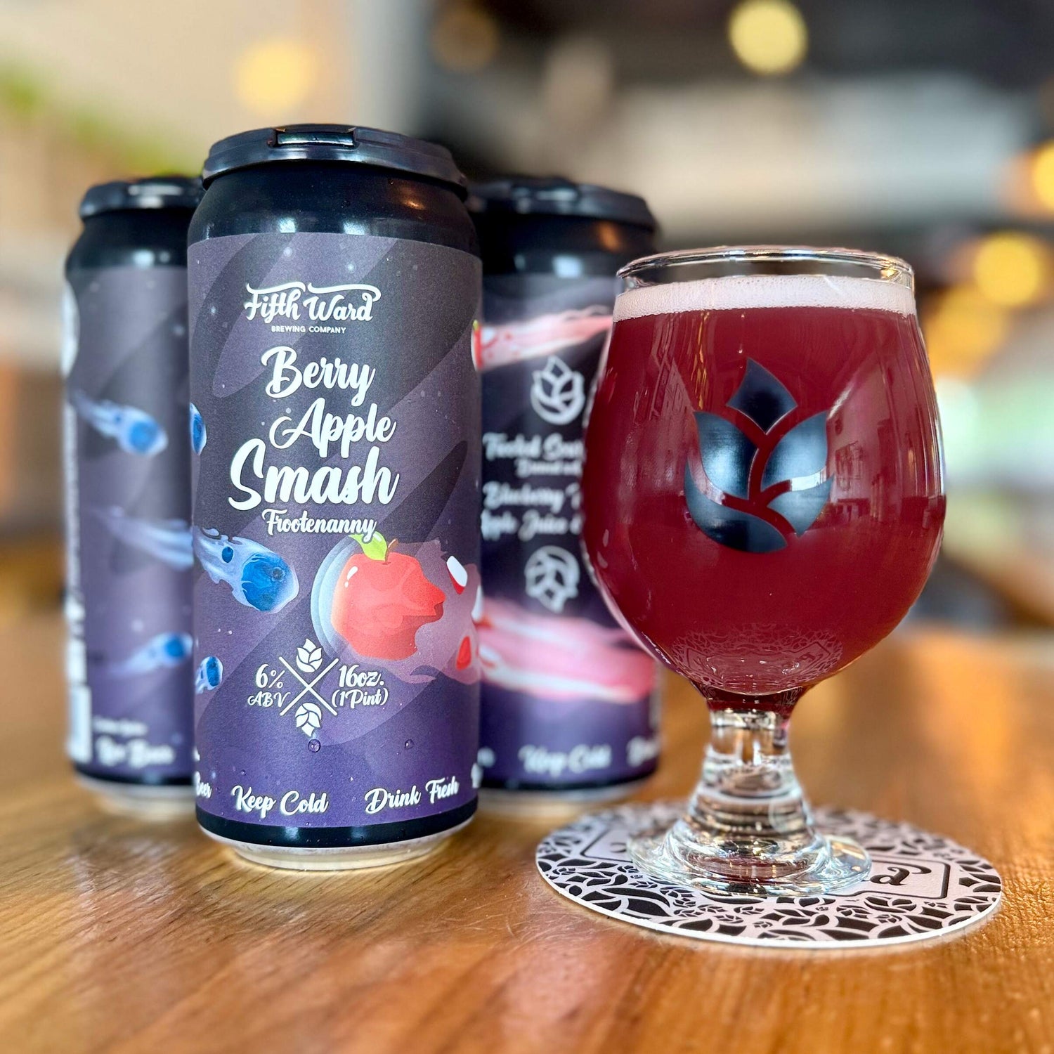glass of red-purple fifth ward berry apple beer next to a six pack