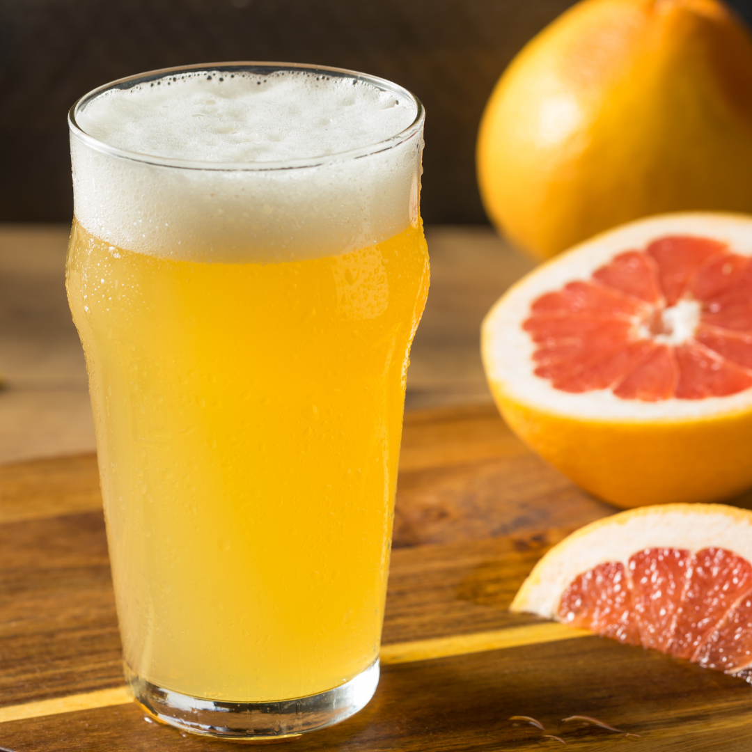 Glass of hazy yellow beer with foamy head next to a cut grapefruit