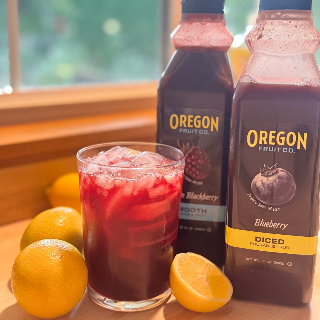 Clear glass of dark red drink next to two plastic bottles surrounded by lemons