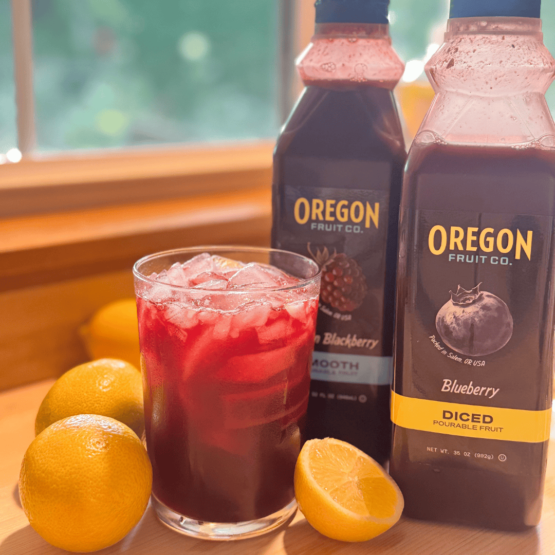 Clear glass of dark red drink next to two plastic bottles surrounded by lemons