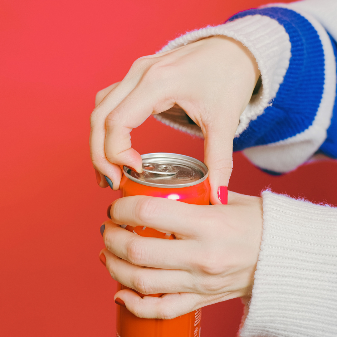 Person in a blue and white striped shirt opens a red can in front of red background