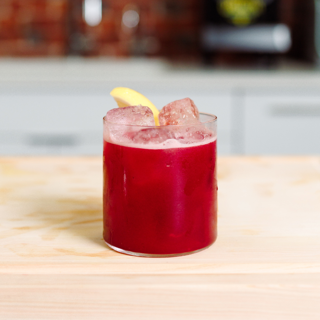 image of a bright red marionberry sour drink in a cocktail glass on a butcher block counter