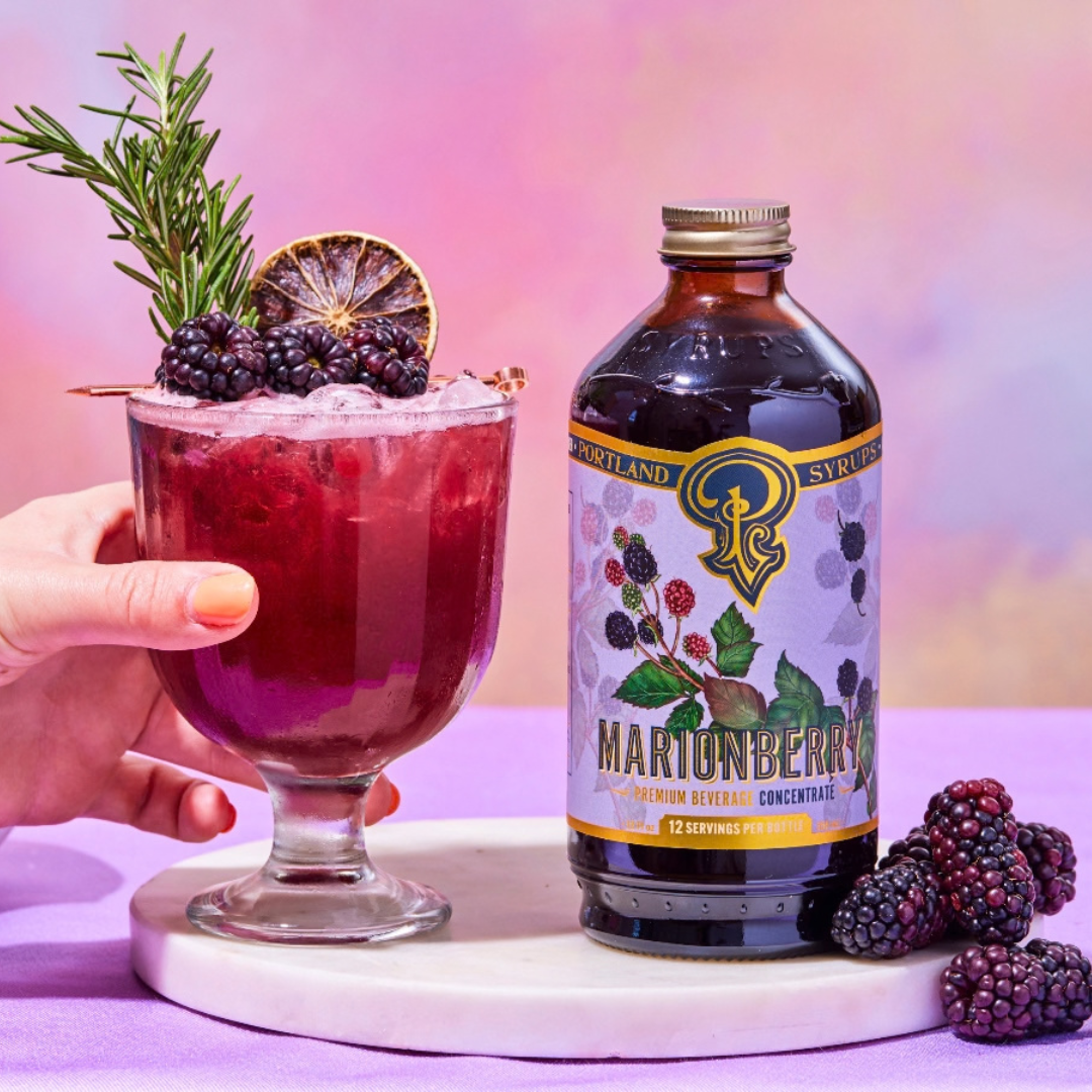 glass of bright red cocktail next to bottle of Portland Syrups on a serving disc