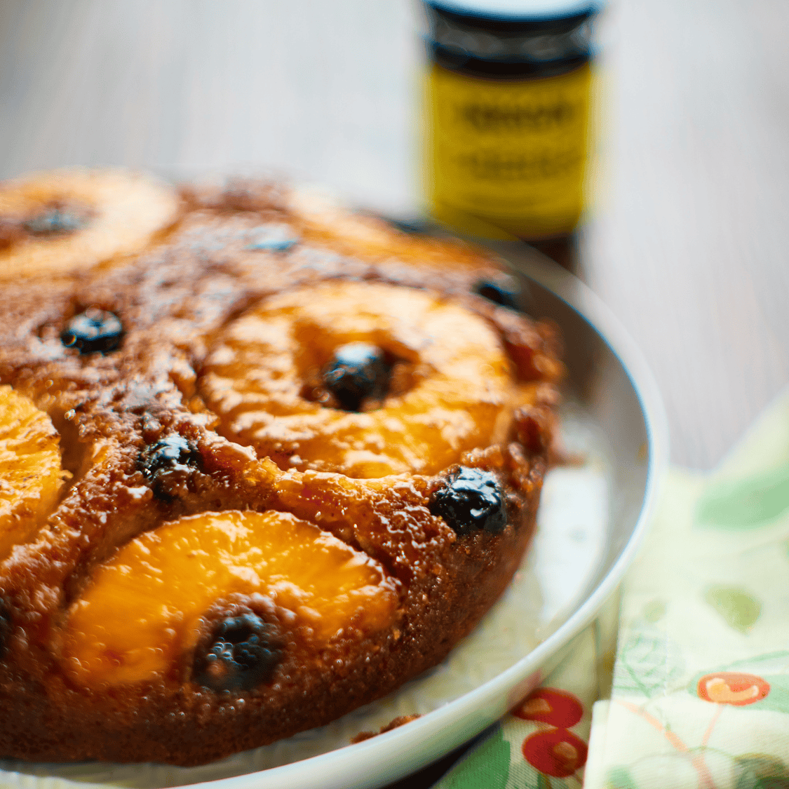 image of pineapple upside down cake with jar of cocktail cherries in background