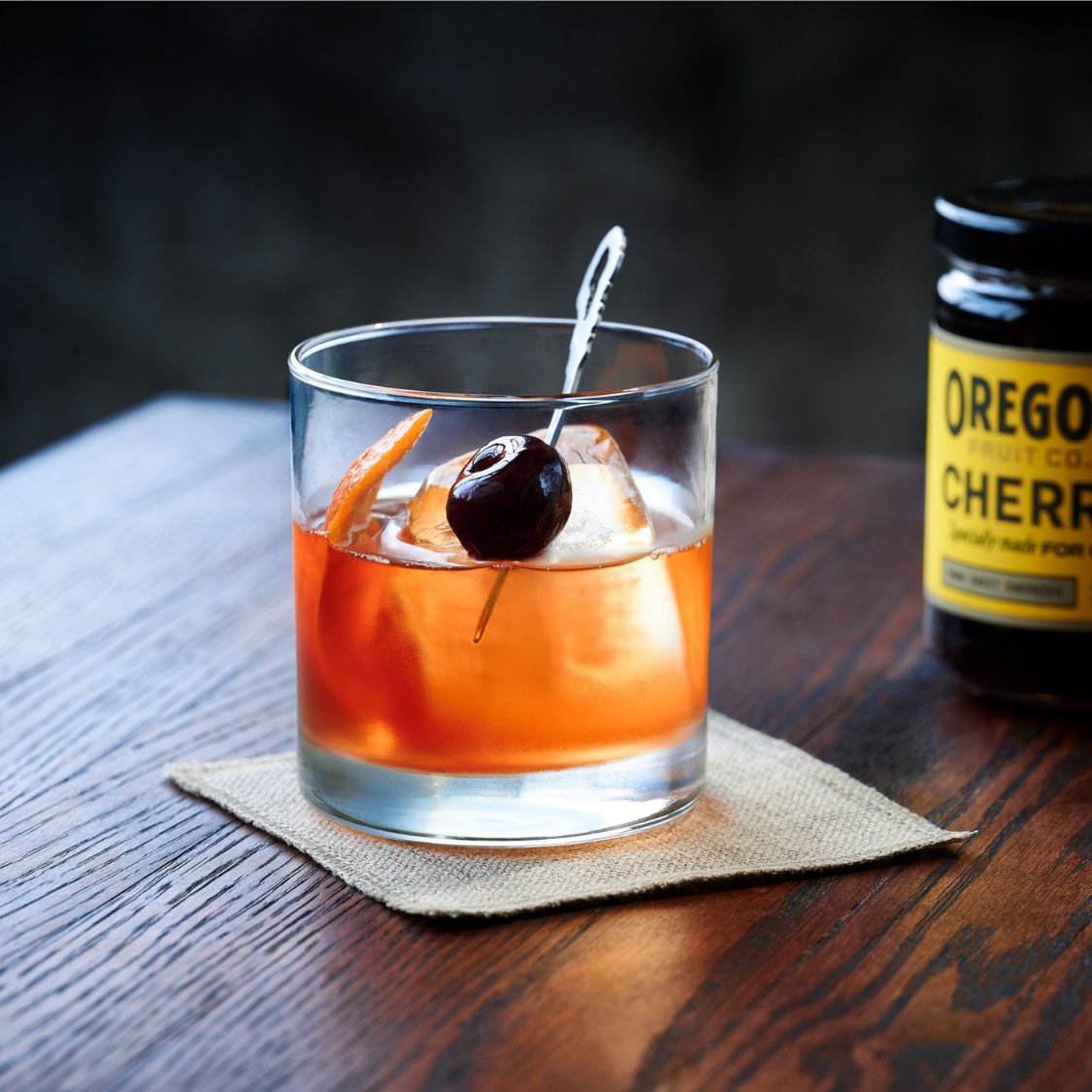 image of a perfect manhattan cocktail in front of a jar of Oregon Fruit cocktail cherries