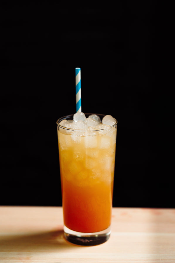 Glass of orange drink with ice and a striped straw on a wooden surface and black background