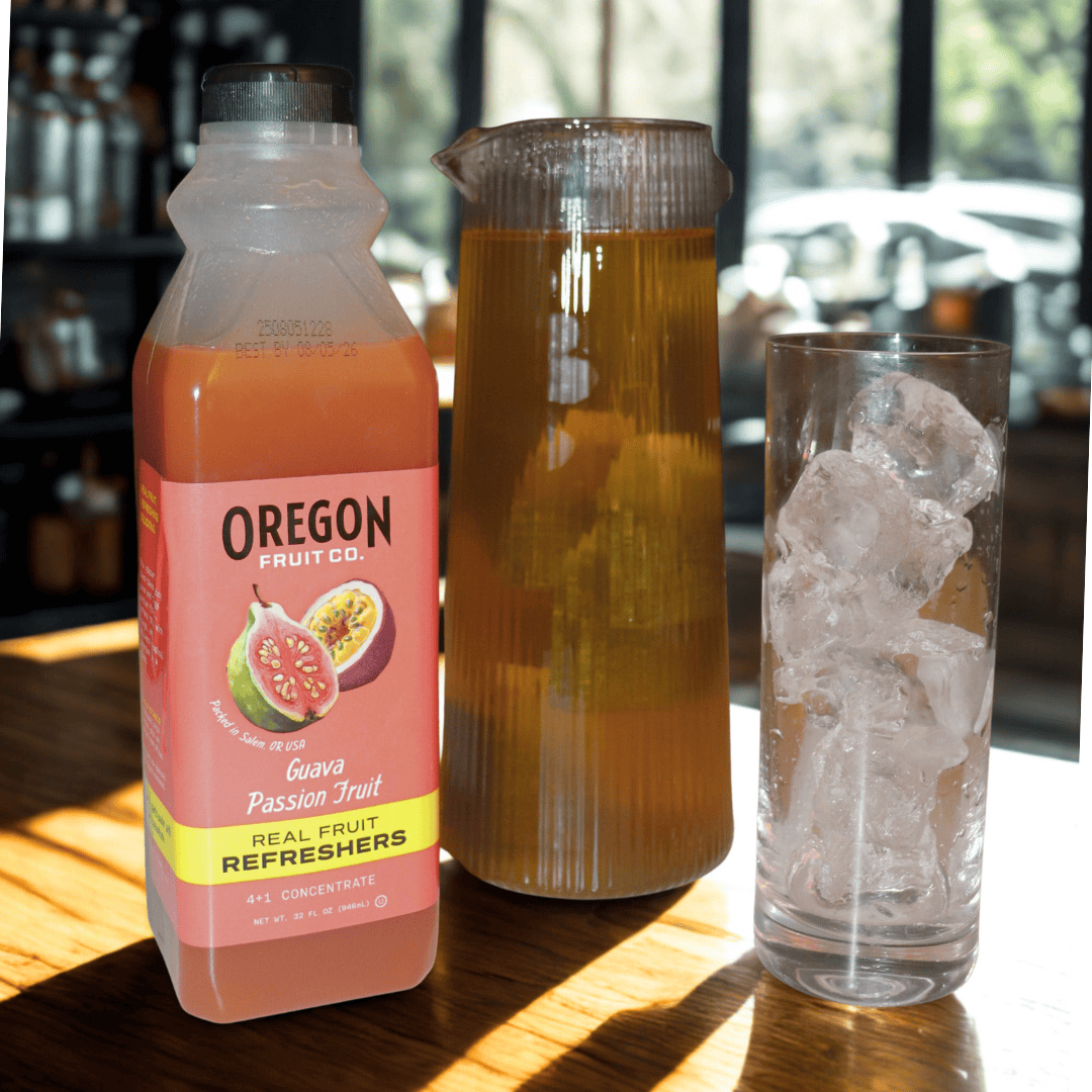 Clear glass of light iced tea next to bottle of Guava Passion Fruit refresher on a wood table in the sun