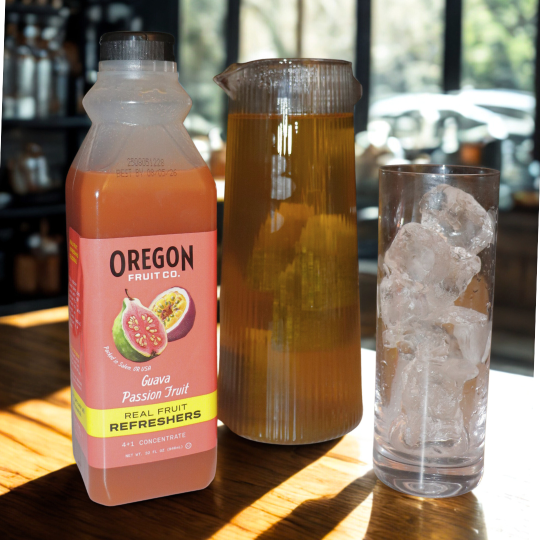 Clear glass of light iced tea next to bottle of Guava Passion Fruit refresher on a wood table in the sun