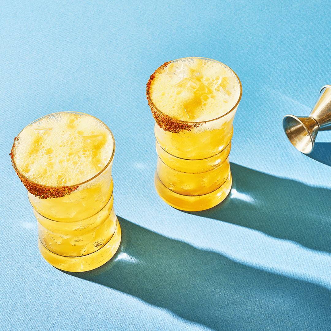 Two cocktail glasses of yellow beverage with a salted rim