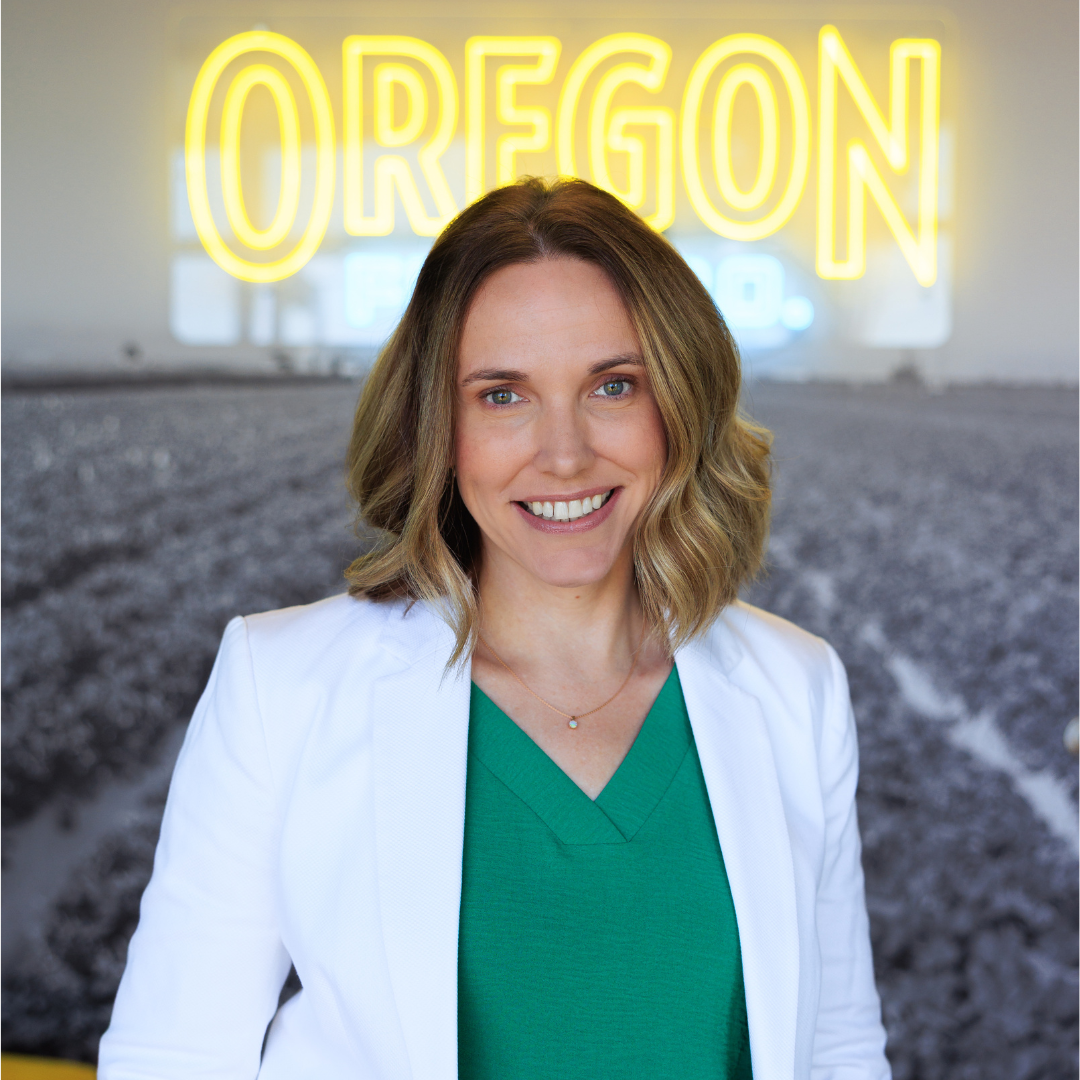 a woman stands in front of a neon sign saying Oregon
