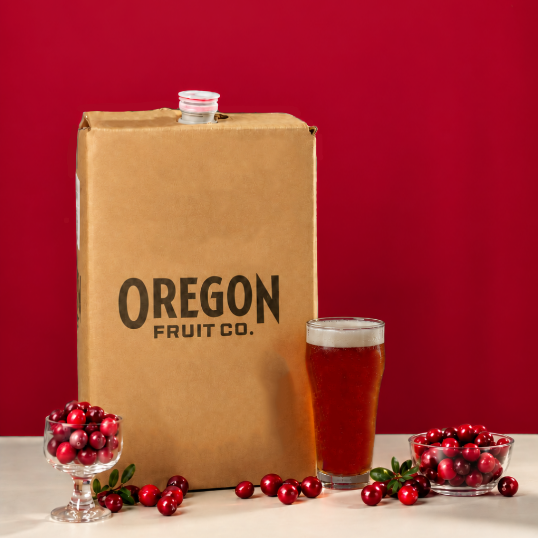 a cardboard box of Oregon Fruit cranberry puree next to a glass of cranberries and a glass of cranberry beer
