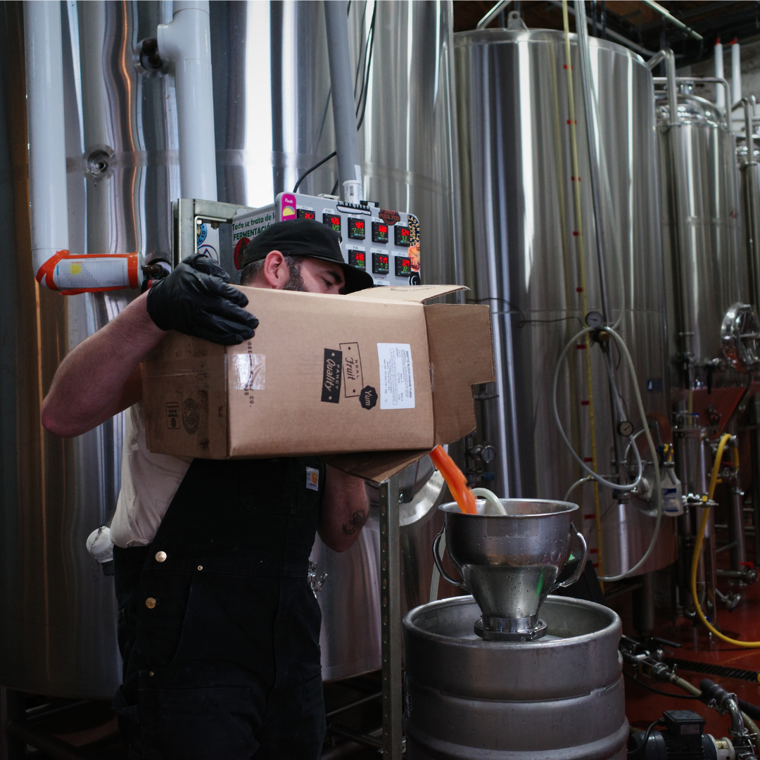 a man pours oregon fruit aseptic puree into a kettle from  a 42lb cardboard box
