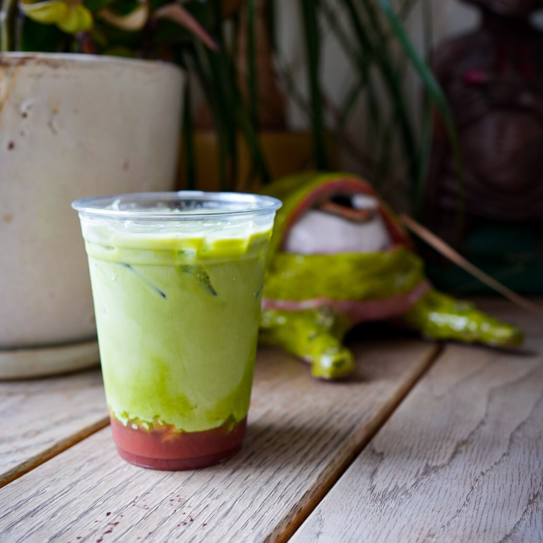 glass of green iced matcha sits on a wood floor in front of a plant