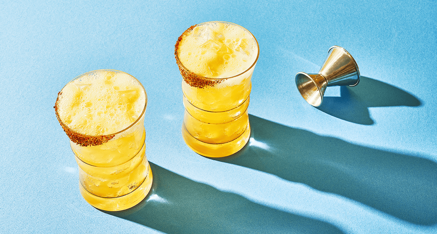 two glasses of yellow liquid with a metal measuring cup