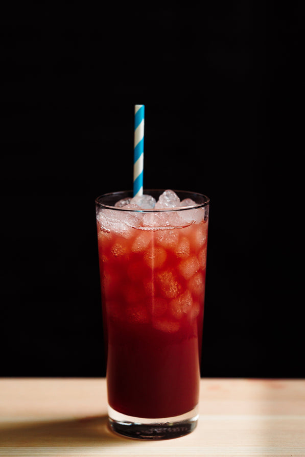 Red drink in glass with ice with a straw on a black background