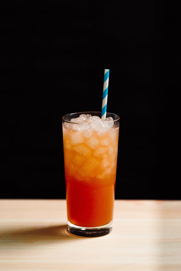 Red drink with ice and a blue straw in a glass on a wooden surface with a black background
