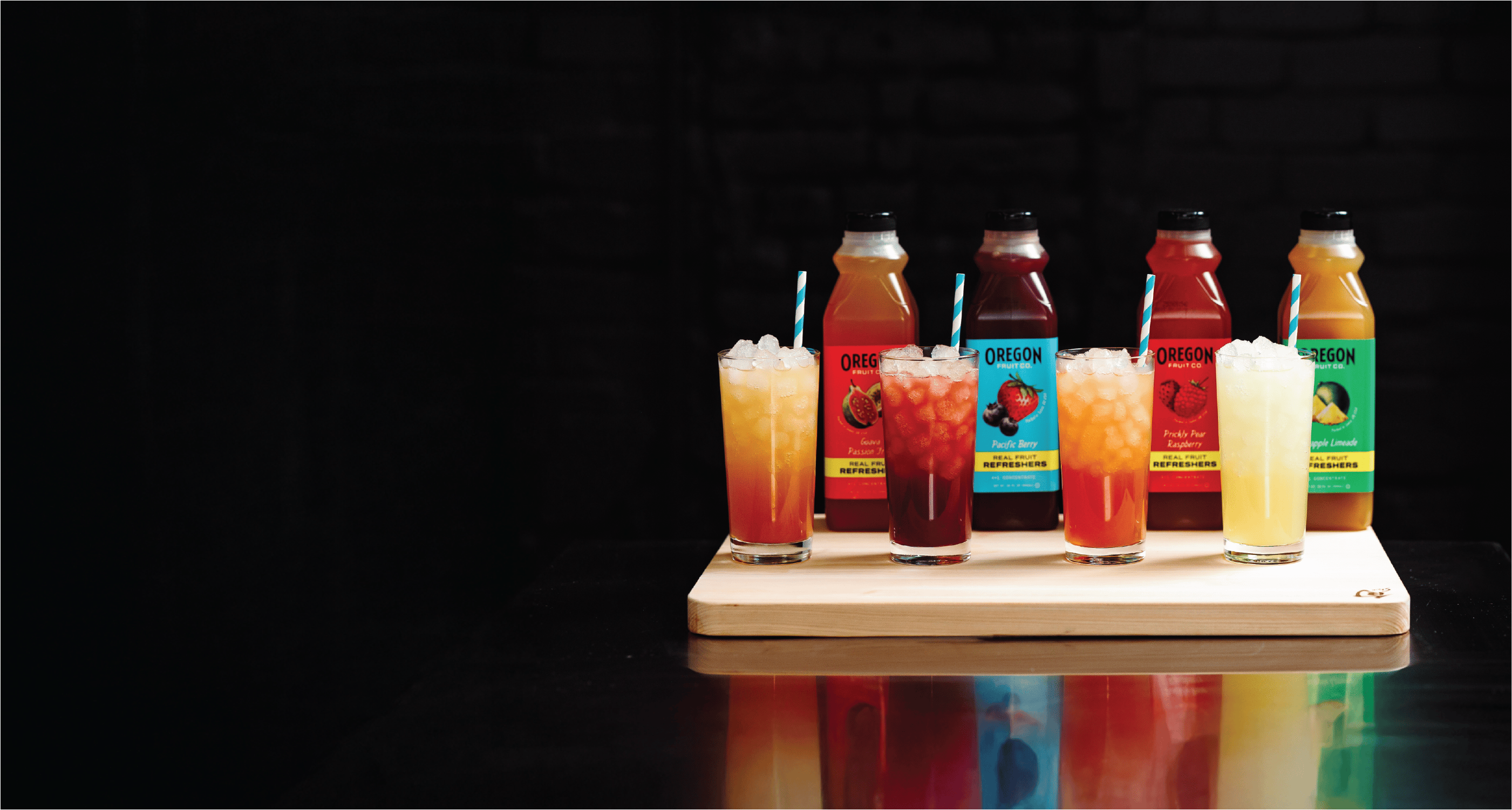 Beverage bottles and glasses on a wooden stand against a dark background